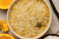 Calendula orange and vanilla bath salts in a bowl with orange, vanilla and calendula surounding them