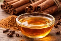 Cinnamon bark essential oil in a bowl with bundles of cinnamon sticks around it