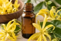 Ylang ylang flowers in a wooden bowl and surrounding the bottle of ylang ylang essential oil