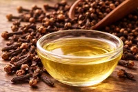 Clove bud essential oil in a bowl on a timber surface with large scoop of clove buds