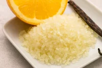 Orange and vanilla bath salts on a white plate with a wedge of orange and vanilla bean